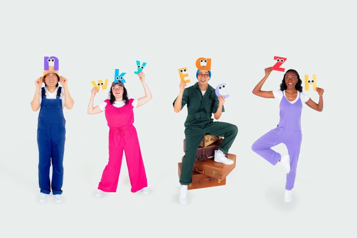 Four people wear brightly color coveralls and hold cut outs of letters above their heads.