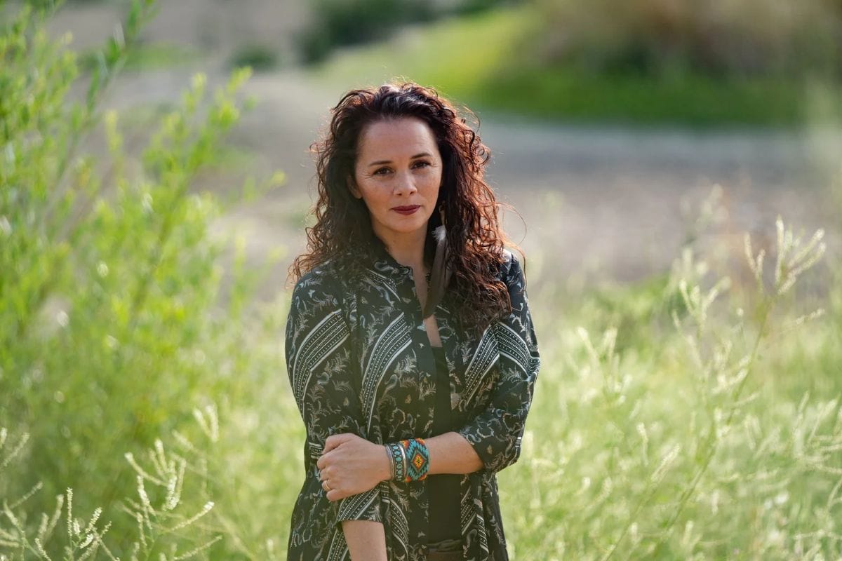 A woman stands in a field with tall plants surrounding her.