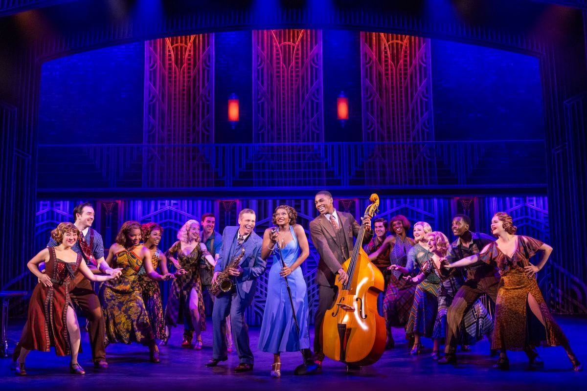 A blue lit art deco background. In the forefront is a group of jazz dancers and musicians.
