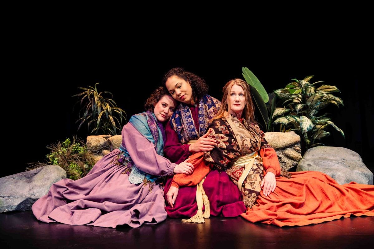 Three women sit together, holding each other.