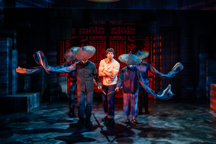 Bruce Lee stand in the middle of four men wearing hats and looking down. Lee has his arms crossed looking angry.