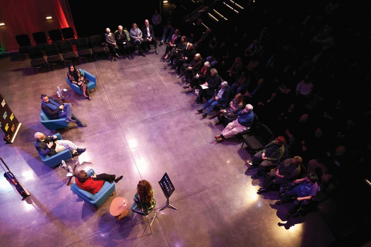 An aerial image showing a group of people sitting in armchairs on the stage with an audience listening to them. 