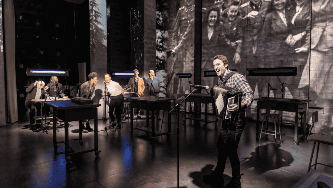 A man in the forefront plays an accordion and sings with backup singers.