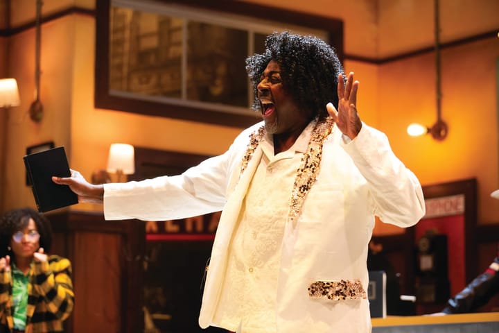 A man wearing a white suit sings with a book in his hand.