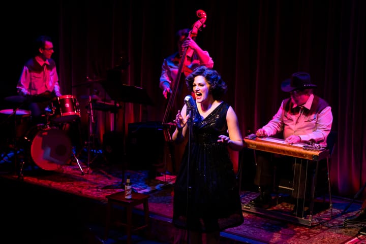 A woman sings on stage in front of a country band.