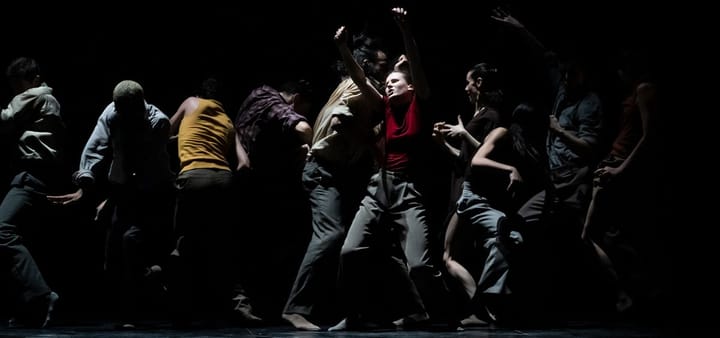 The Paris Opera Ballet performs. Men and women dancers wear everyday clothes and are in a line in different movem