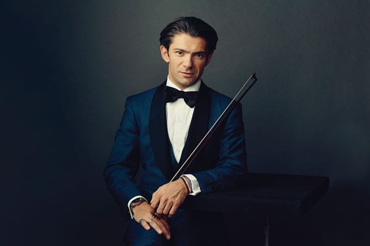 Cellist Gautier Capuçon wears a blue tux and holds his instrument, looking at the camera.
