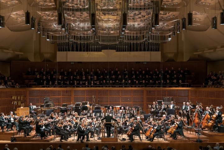 A symphony plays on stage with a large chorus in the back.