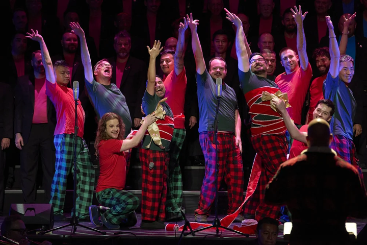 A chorus of men on stage wear pajamas and have their arms raised as they sing.