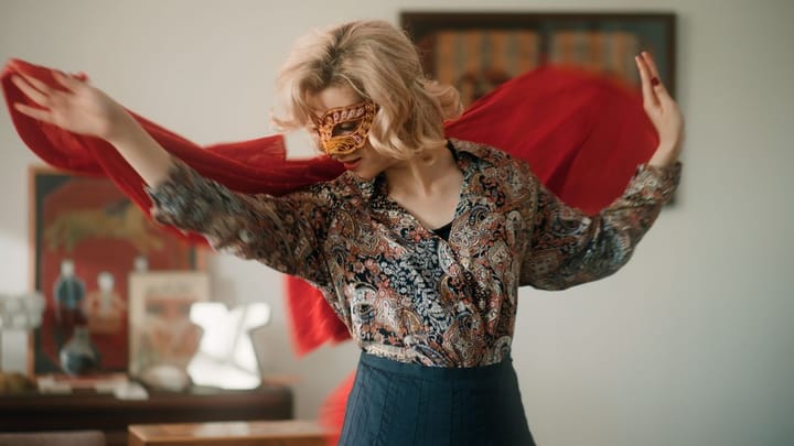 A woman in a mask dances in a room with a scarf.