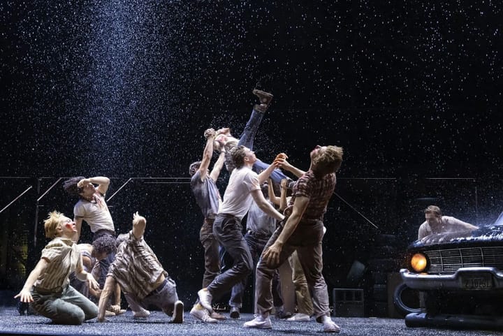 A group of boys fall backwards as rain falls on them. A car is in the corner of the image.