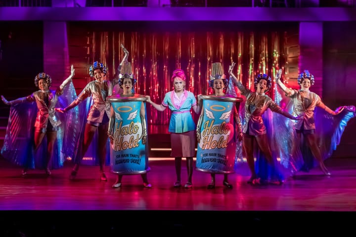 Two women are dressed as hairspray cans and others are dancing in salon garb.